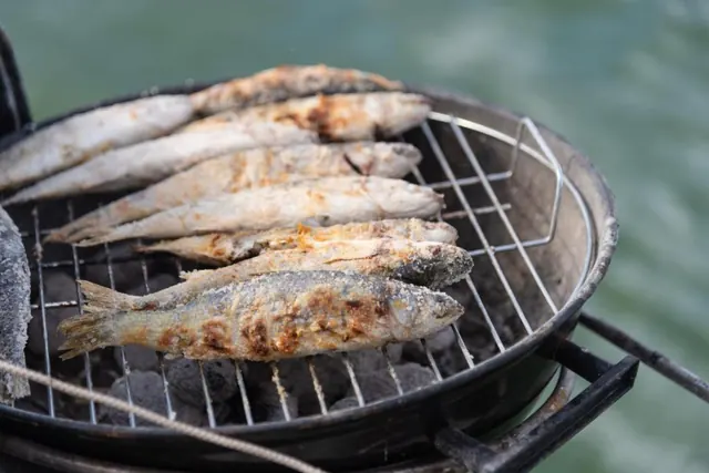 Fresh fish grilling on a kettle braai beside the water